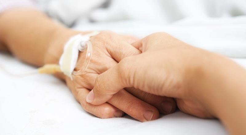 Image of someone holding patient hand in hospital.