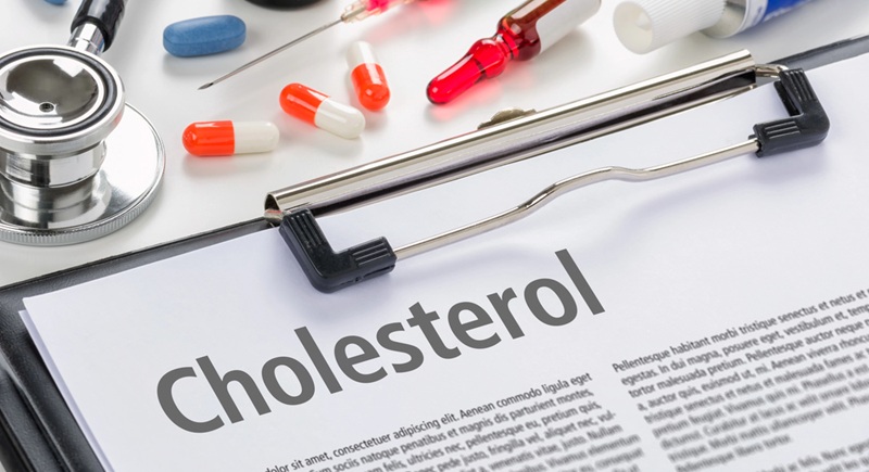 Image of a doctor's desk with stethoscope and pills and a clipboard with a document titled CHOLESTEROL on it.